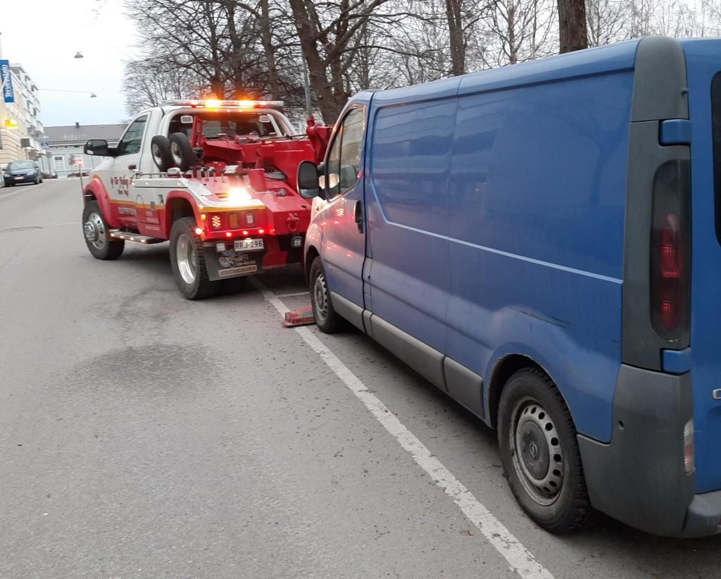 Hinausauto ottamassa pakettiautoa hinaukseen pysäköintiruudusta.