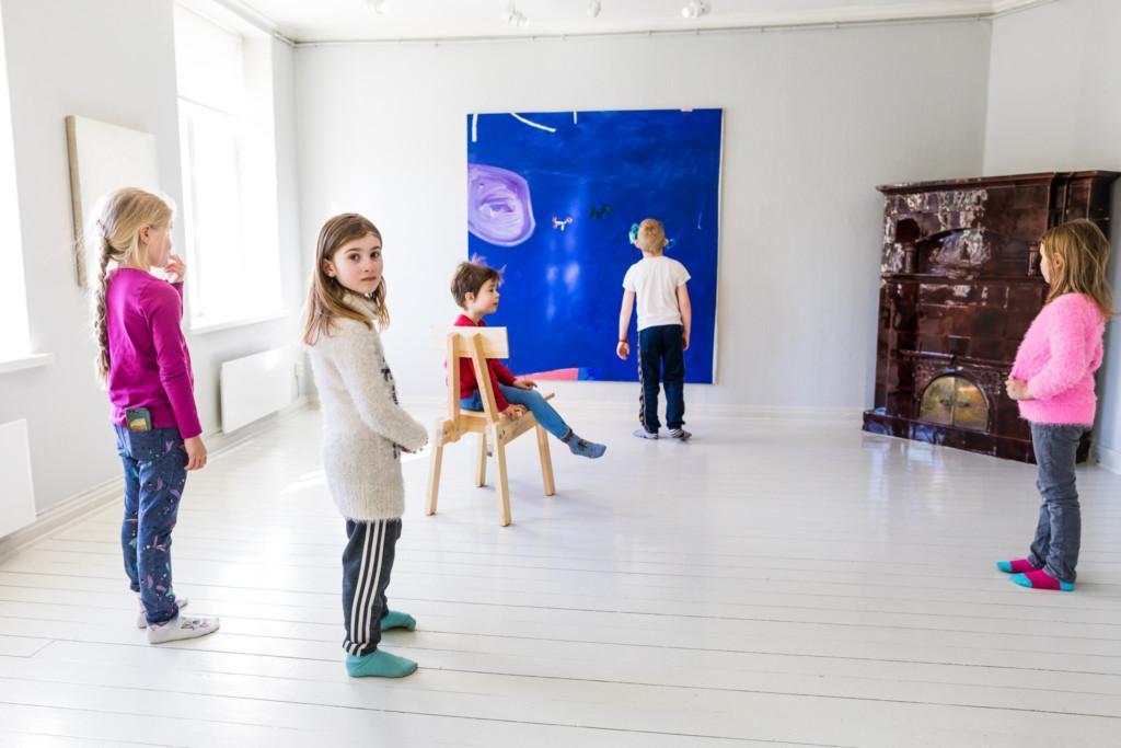 5 alakouluikäistä lasta tutustuvat maalauksiin valoisassa näyttelytilassa.