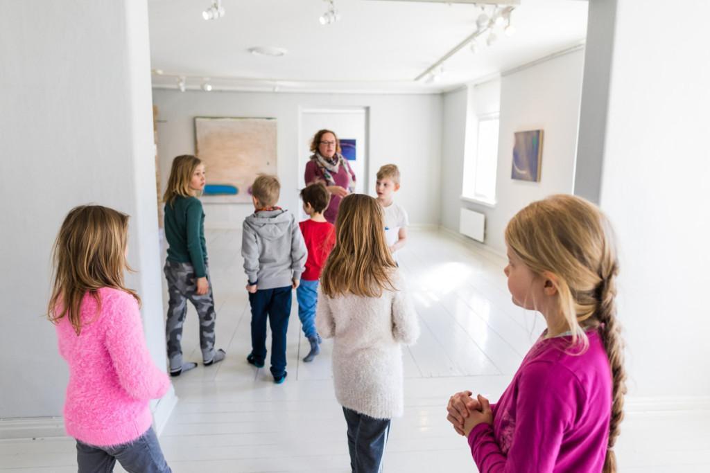 7 alakouluikäistä lasta opettajan kanssa taidenäyttelyssä.