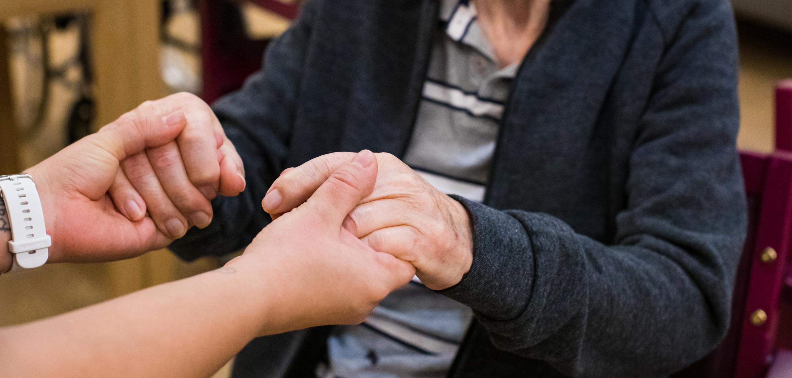 En äldre och en yngre person håller varandras händer