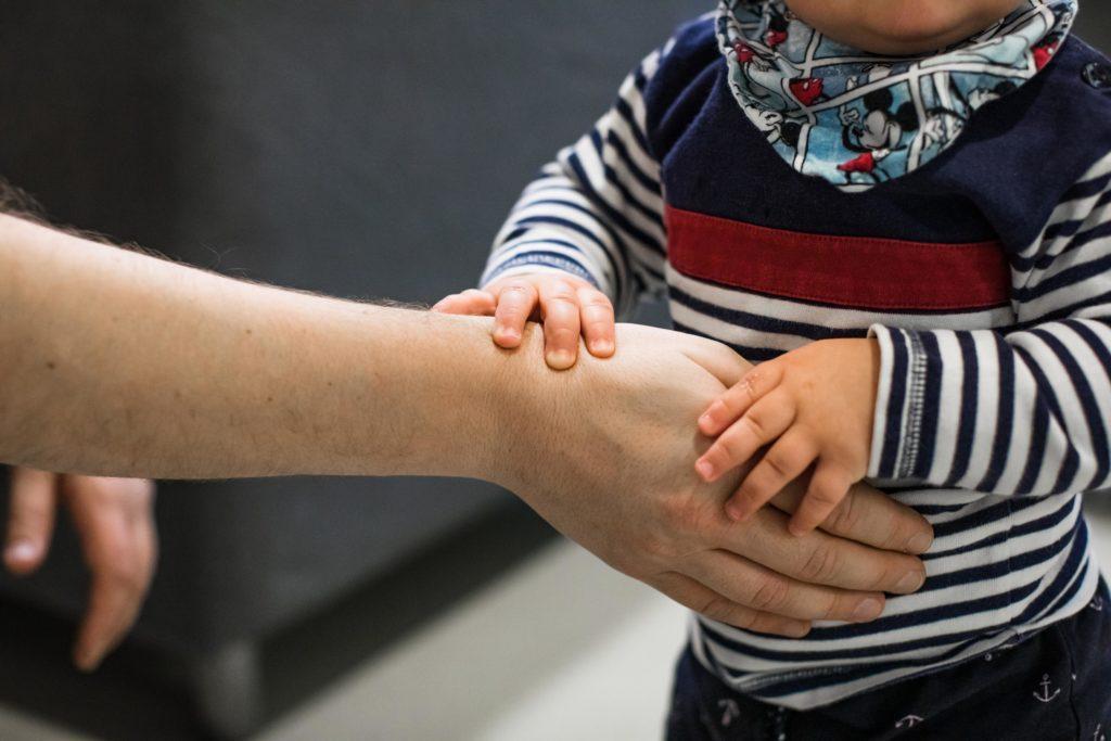 Ett litet barn håller en vuxens hand.