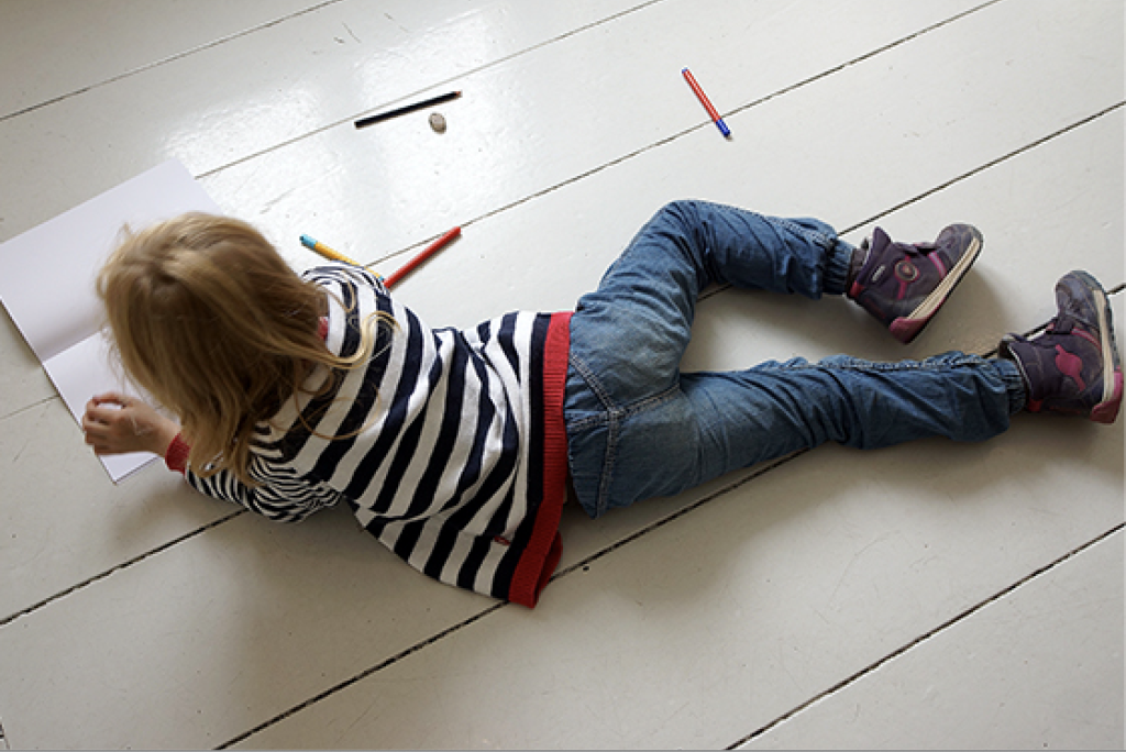 Lapsi makaa lattialla ja piirtää.