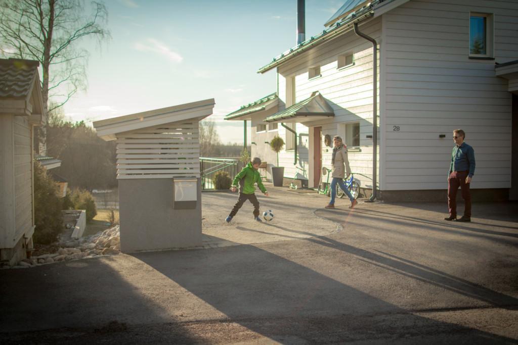 En familj spelar fotboll på gården i kvällssolen.