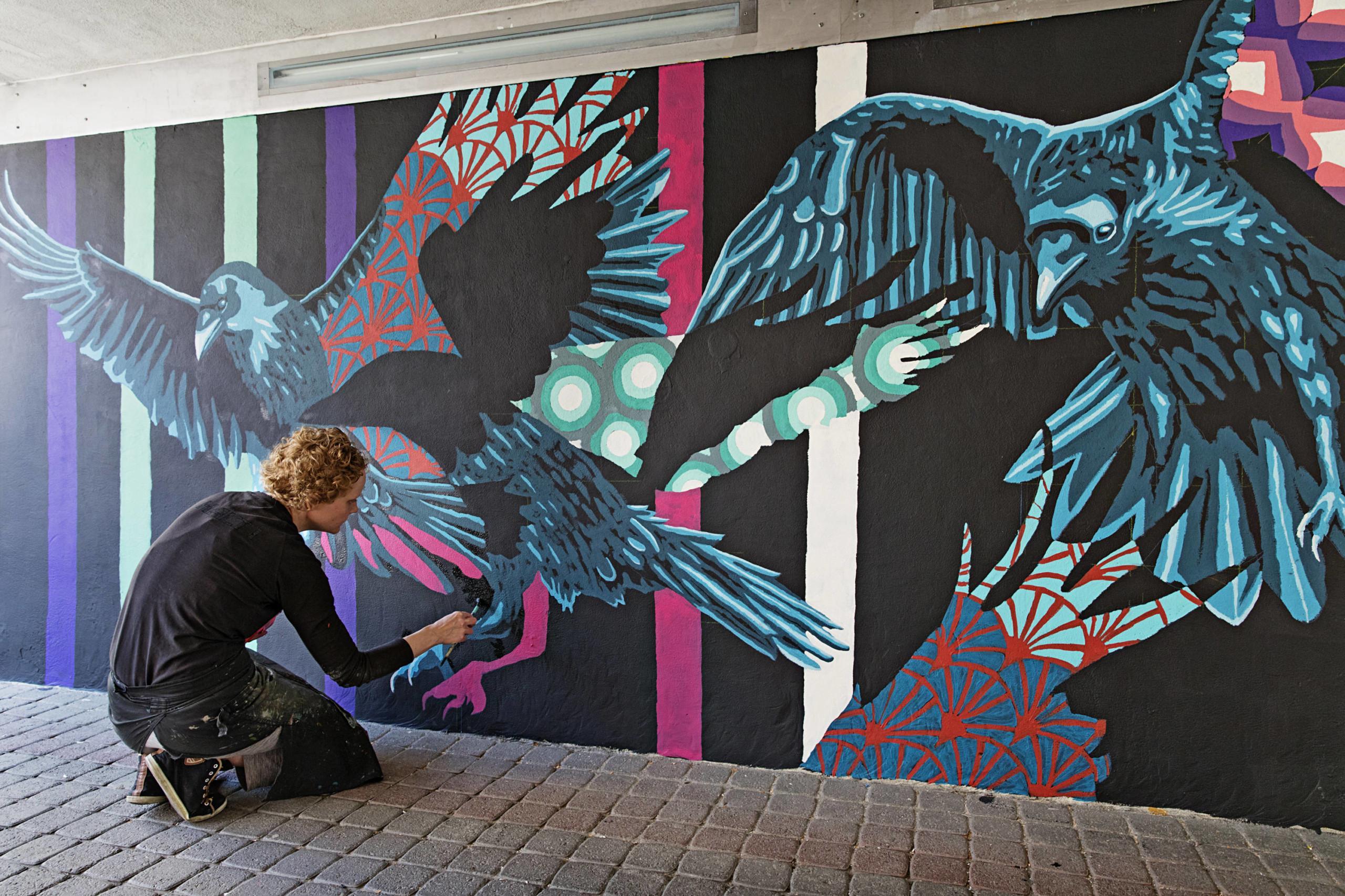 Nainen maalaa seinälle lintuja.