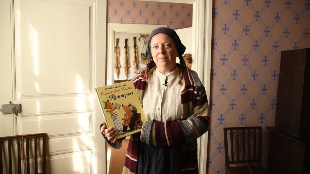 Vanhanaikaisesti pukeutunut nainen pitää käsissään satukirjaa