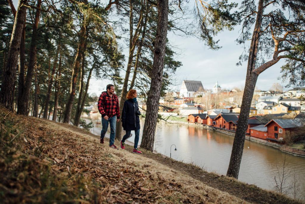 En man och en kvinna promenerar på Näsebacken, röda strandbodar ses i bakgrunden.