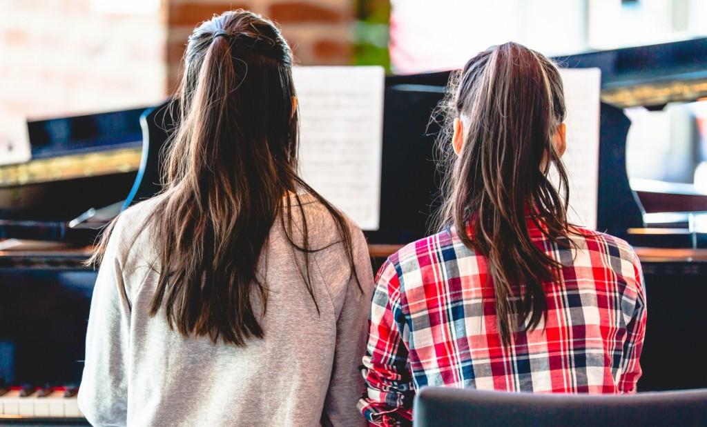 Kaksi tyttöä soittaa pianoa yhdessä vierekkäin.