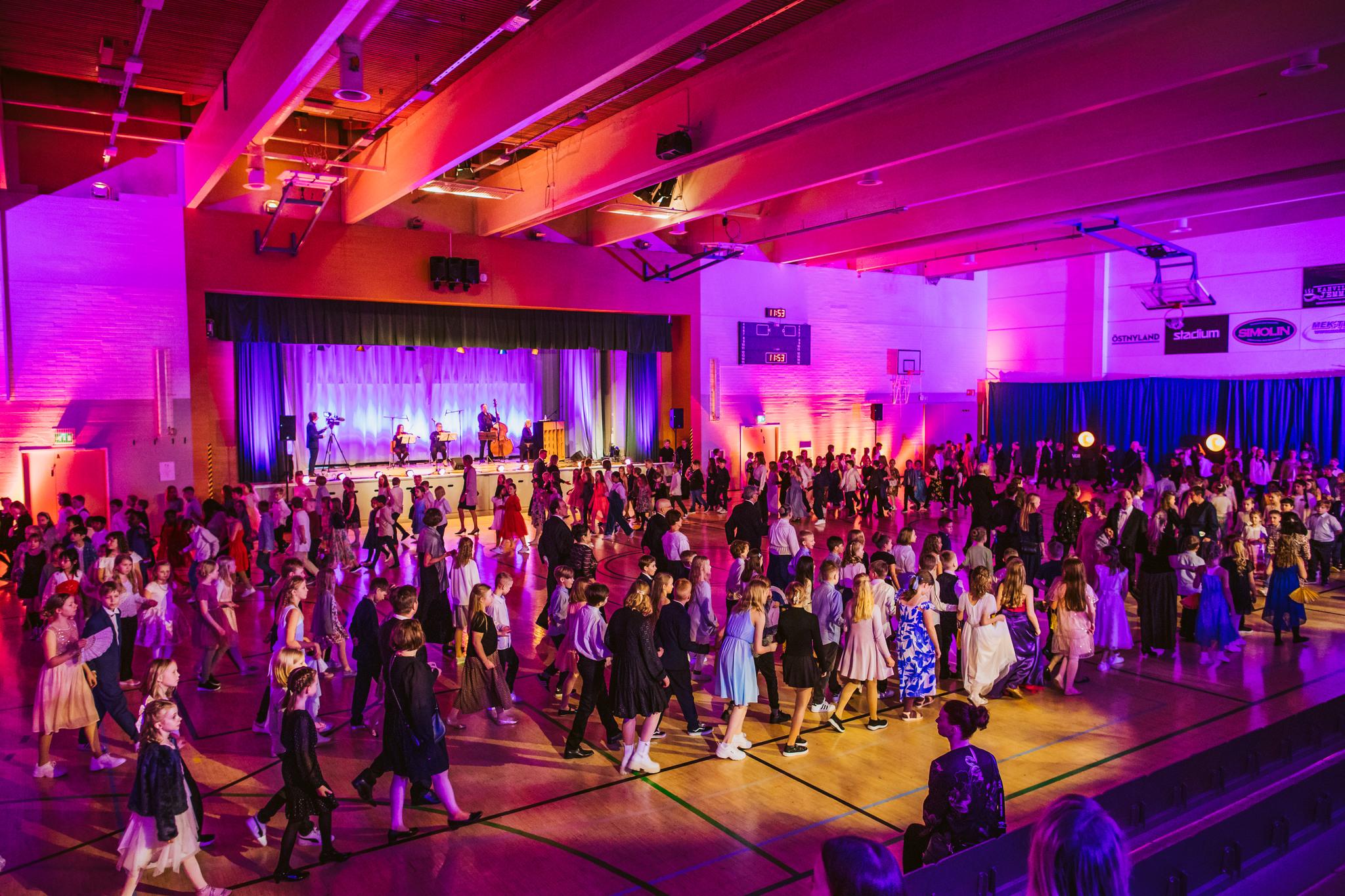 Fint upplyst idrottshall, på scenen en orkester som spelar, på dansgolvet barn som dansar. Borgå, Barnens lantdagsbal 2023