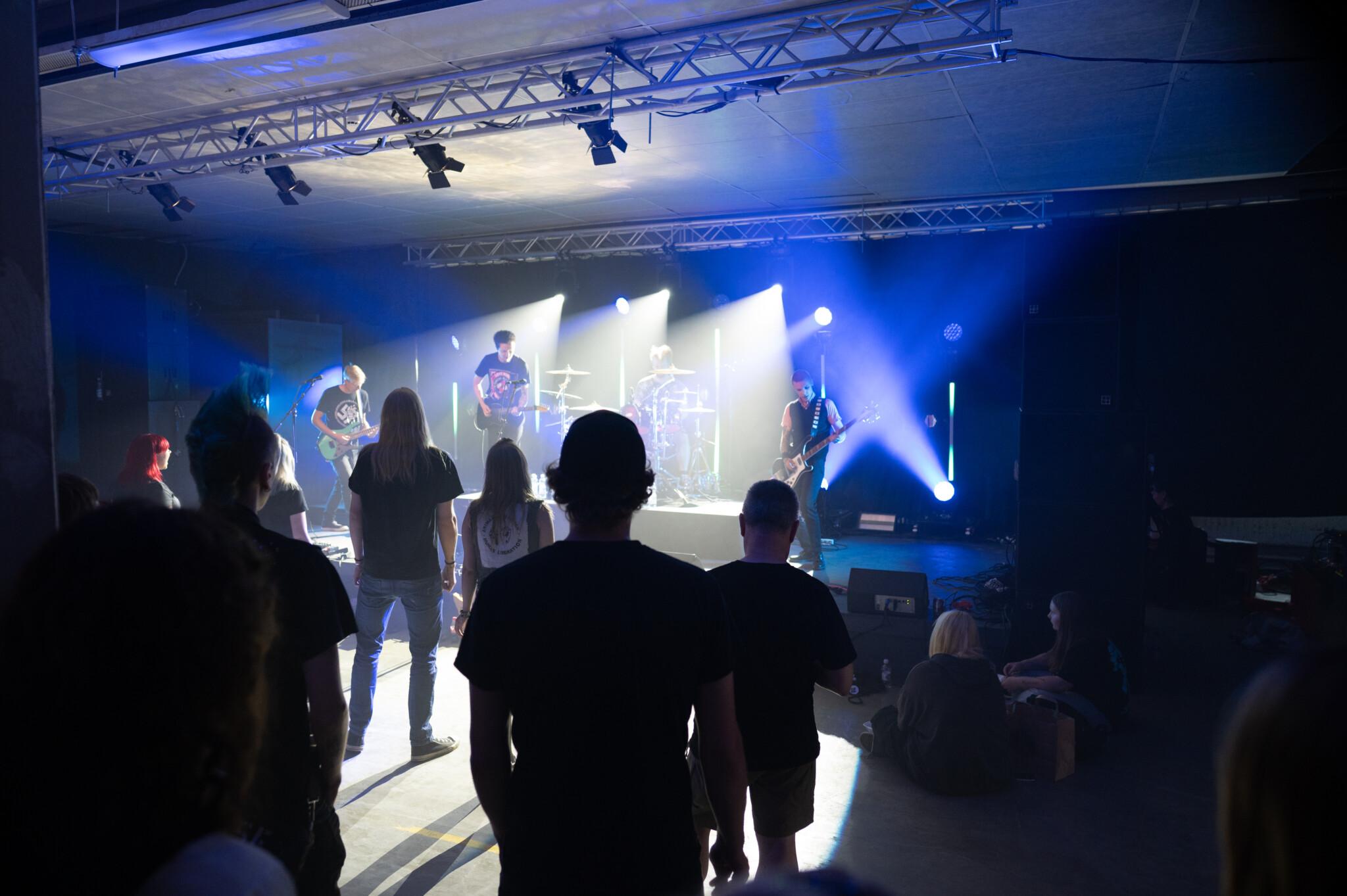 Rokkiklubimainen sisätila, yleisö seisoo lavan edessä, lavalla rokkibändi soittaa.