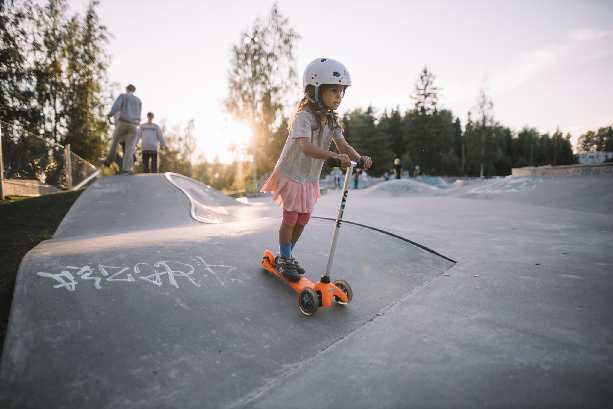 A little girl on a kickboard in a skatepark.