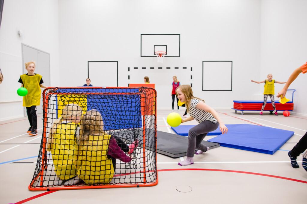 Skolbarn spelar bollspel i skolas gymnastiksal.