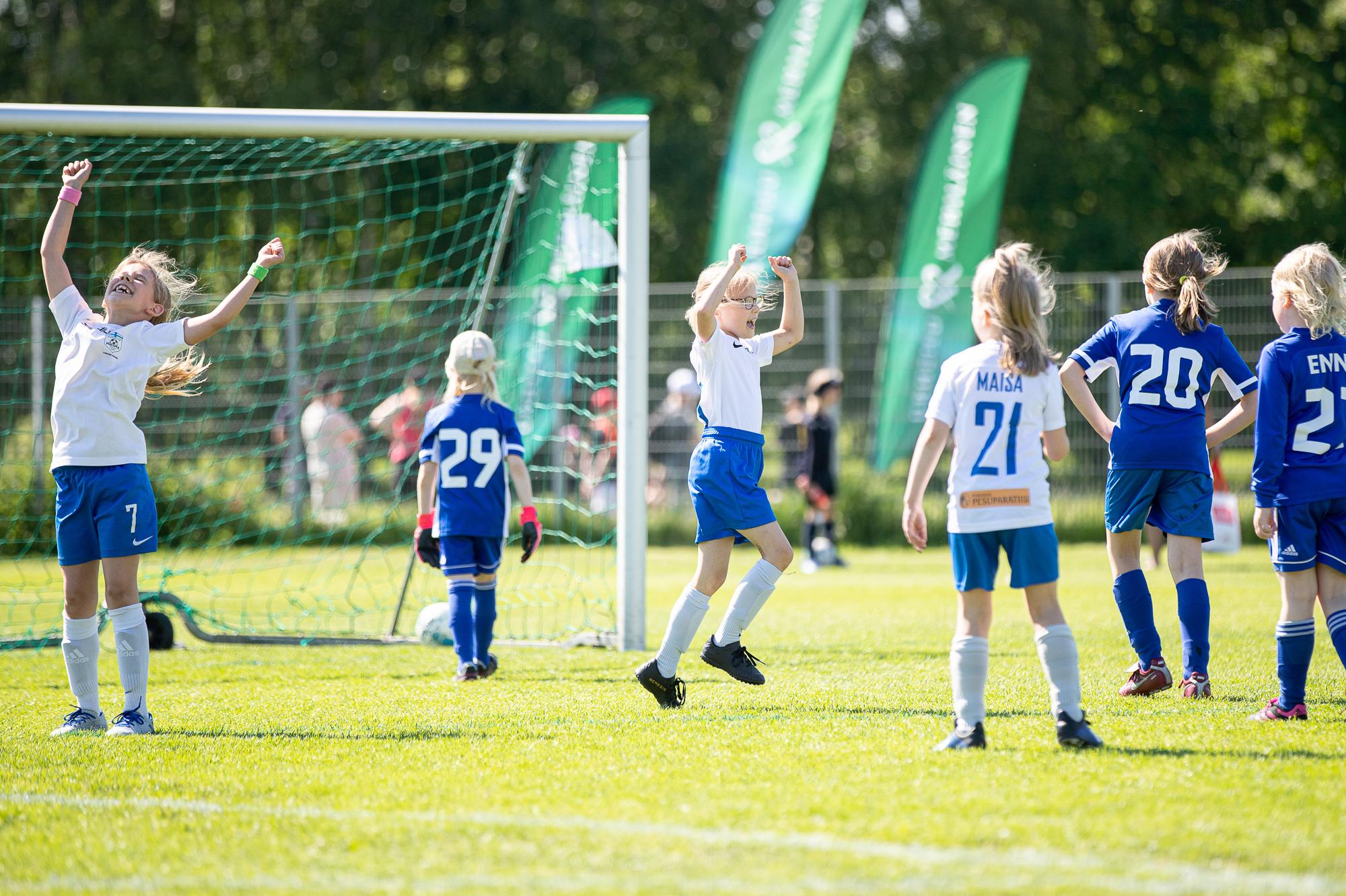 Pienet tytöt tuulettavat jalkapallon parissa.
