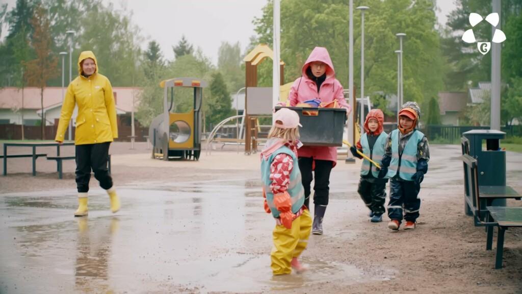 Päiväkodin pihalla opettajat ja lapset leikkivät vesisateessa.