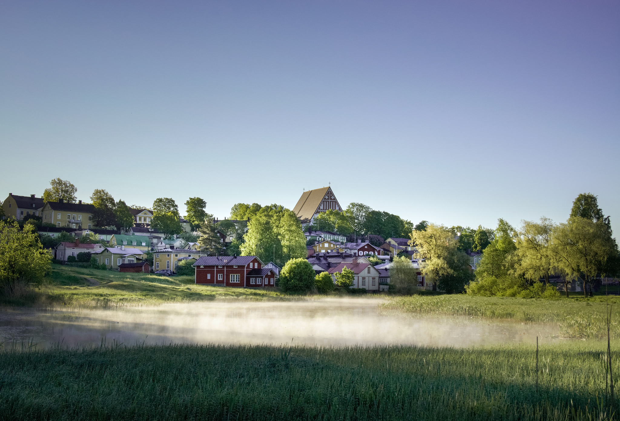 Old Porvoo seen from across the river, with morning mist over the river, and trees are bright green in the spring.