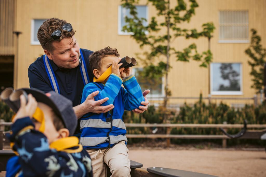 Pojat kiikaroivat itse askartelemilla kiikareilla lastenhoitajan sylissä.