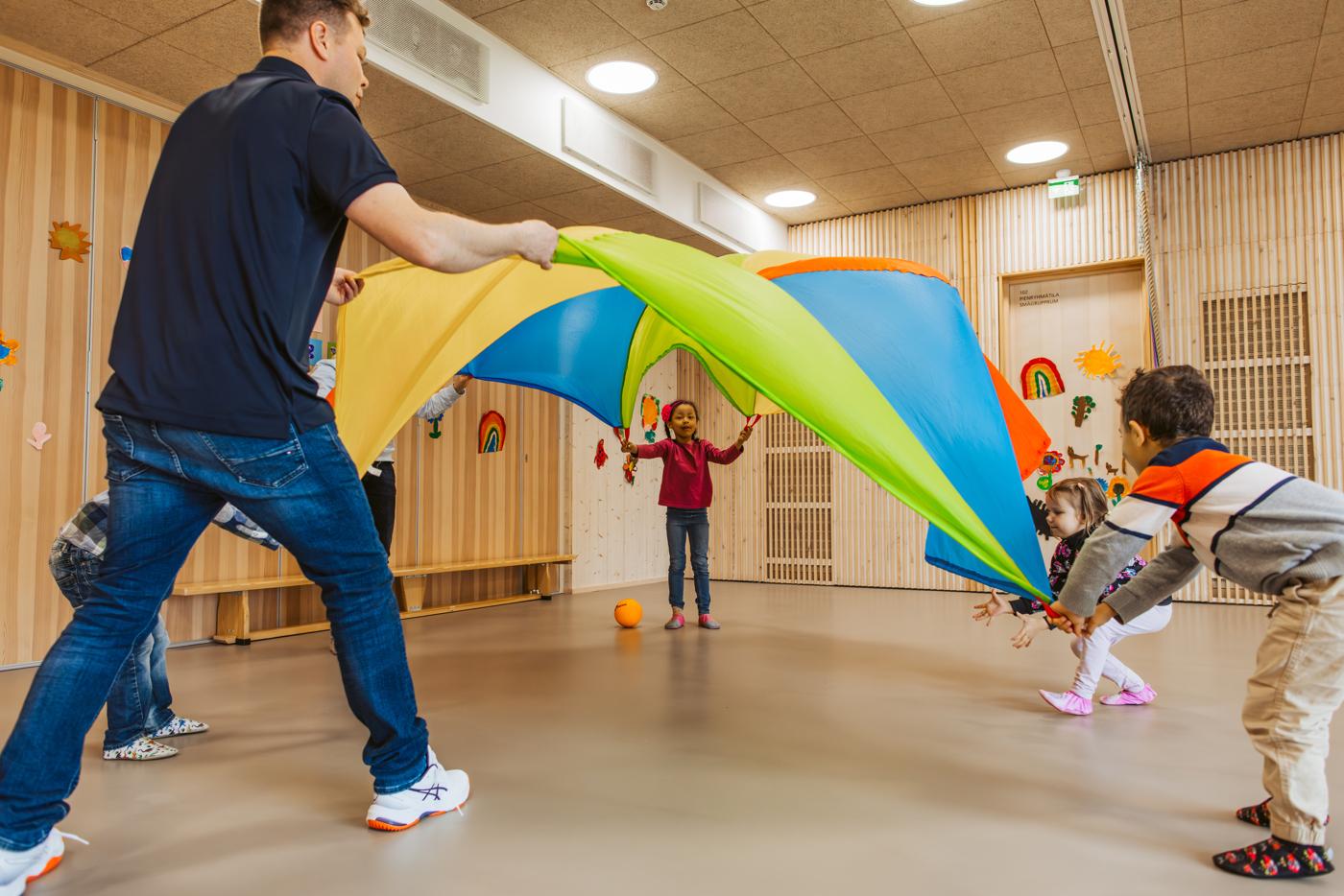 Lapset ja ohjaaja lennättävät leikkivarjoa.