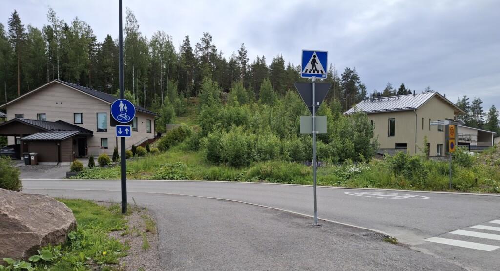 Valokuva rakentamattomasta tontista osoitteessa Påvalsbackankatu 1. Tontilla kasvaa pensaikkoa. Tontin vieressä näkyy naapureiden omakotitalot, tontin takana on metsä.