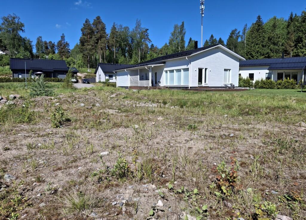 Ett foto. I förgrunden ligger den tomma tomten på Röjarevägen 10a, dit man har fört fyllnadsmassor. I bakgrunden syns enplans egnahemshus i grannskapet.