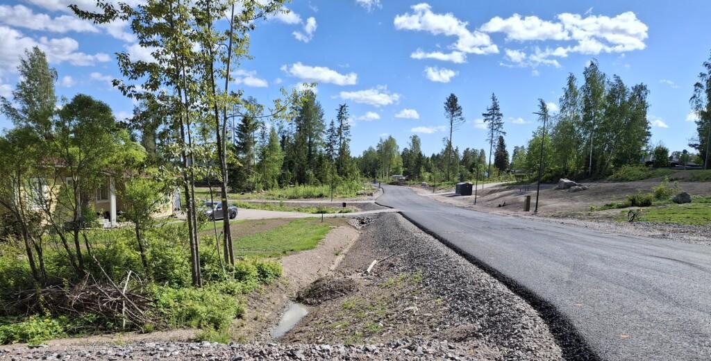 Valokuva. Keskellä uusi asfaltoitu Skaftkärrintie, edessä vasemmalla yksikerroksinen talo, kadun varren muut tontit ovat tyhjiä. Oikealla puolella lähimmät tontit ovat rinteessä.