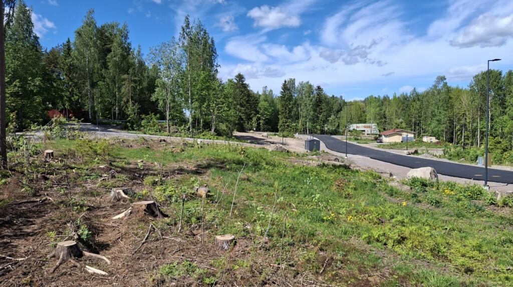 Valokuva. Etualalla tyhjiä tontteja, taaempana Skaftkärrintie ja muutama talo. Maisemassa myös alkukesän vihreyttä ja puustoa.