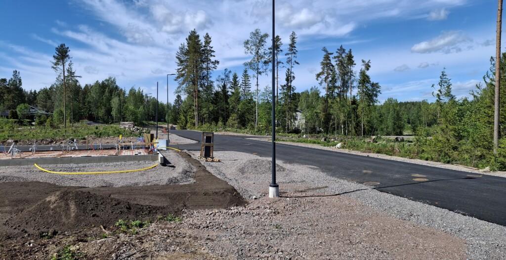 Valokuva. Skaftkärrintien ensimmäisen uuden talon perustukset ja tyhjiä tontteja. Taaempana puiden välistä pilkottaa pari omakotitaloa.