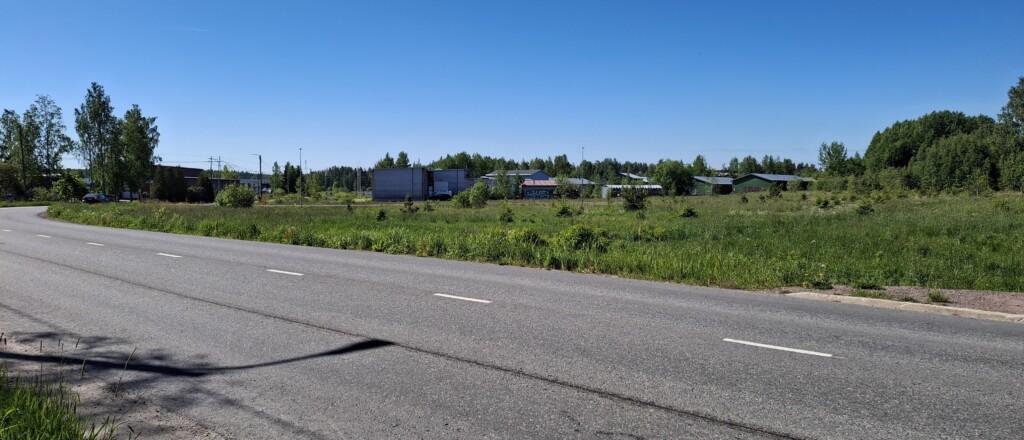 Valokuva niitystä, missä sijaitsee neljä tyhjää yritystonttia. Niityn takana teollisuushalleja ja täysikasvuista puustoa, edessä Pienteollisuustie.