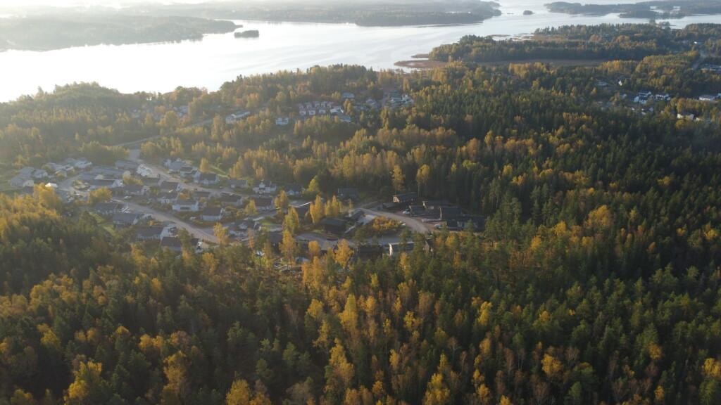 Ilmakuva, omakotitaloja ja muutama tyhjä tontti metsän ympäröimällä alueella. Kauempana lisää pientaloja ja merta.