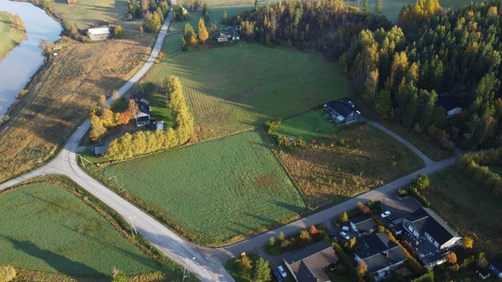 Flygfoto. Två obebyggda tomter på en före detta åker. Runt omkring finns åkrar, egnahemshus och träd. I bildens övre vänstra hörn syns Borgå å.