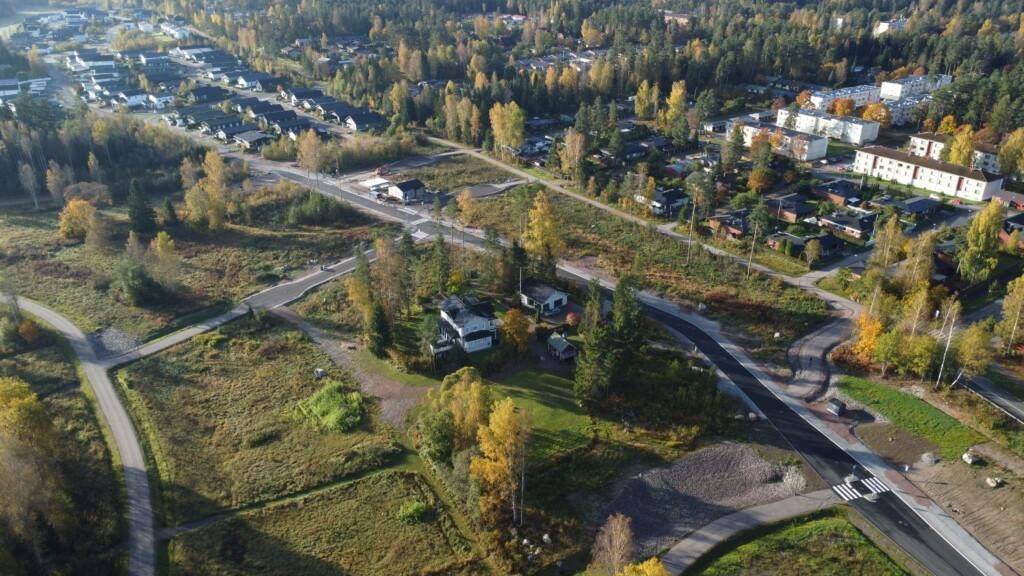 I förgrunden på flygfotot syns nya gator samt gång- och cykelvägar, tomma tomter och några hus. I bakgrunden till vänster syns redan bebyggda småhus i Vårdalen och till höger egnahemshusen i Vårberga, samt längre bort låga höghus.