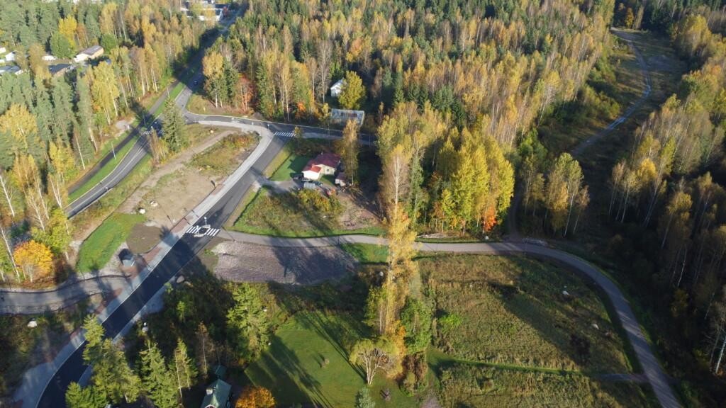 Flygfoto av obebyggda tomter badande i klart höstsolsken. I bilden syns också några äldre egnahemshus och skog.