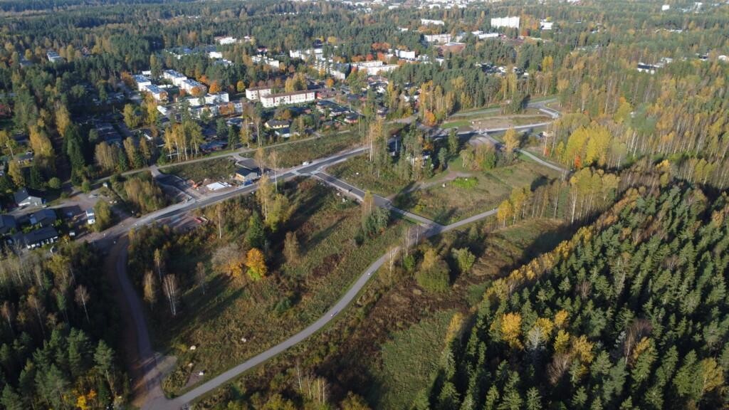 Flygfoto. Några hus under uppbyggnad, mycket obebyggd tomtmark mellan nya gator och gång- och cykelvägar. Framme till höger syns ett landskap med ängar och skog. I bildens bakgrund syns småhus och flervåningshus omgivna av riklig träd.