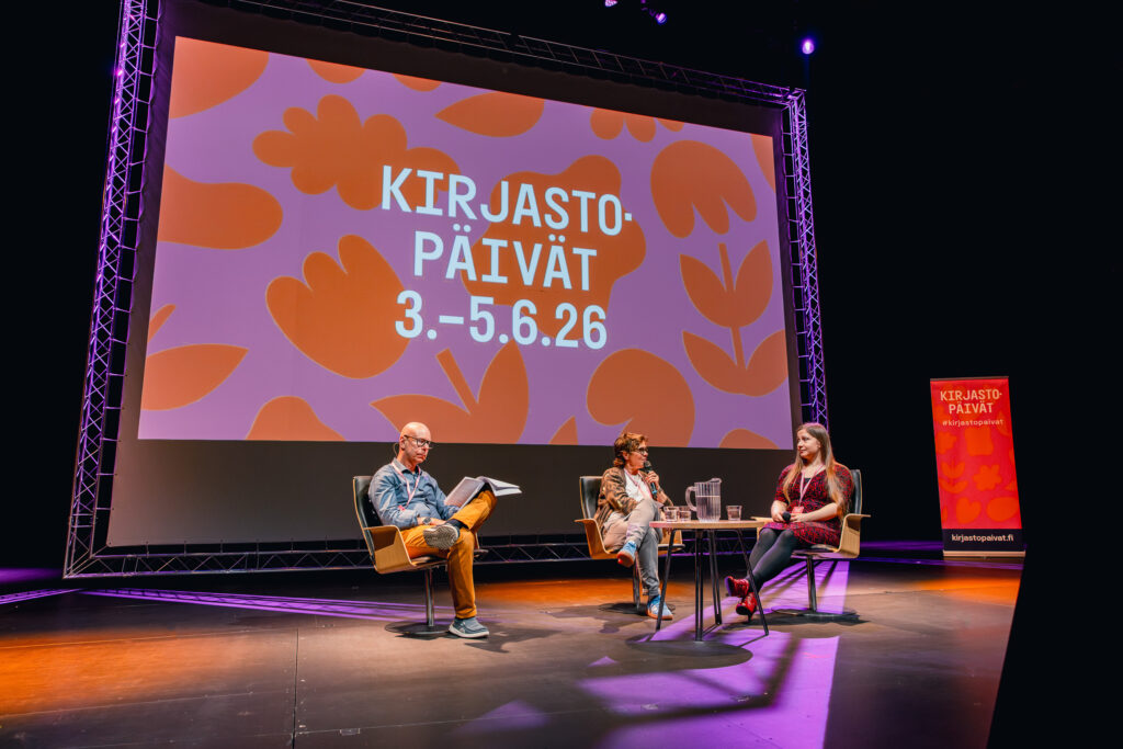 Kolme henkilöä istuu screenin edessä ja teksti Kirjastopäivät 3.-5.6.26.