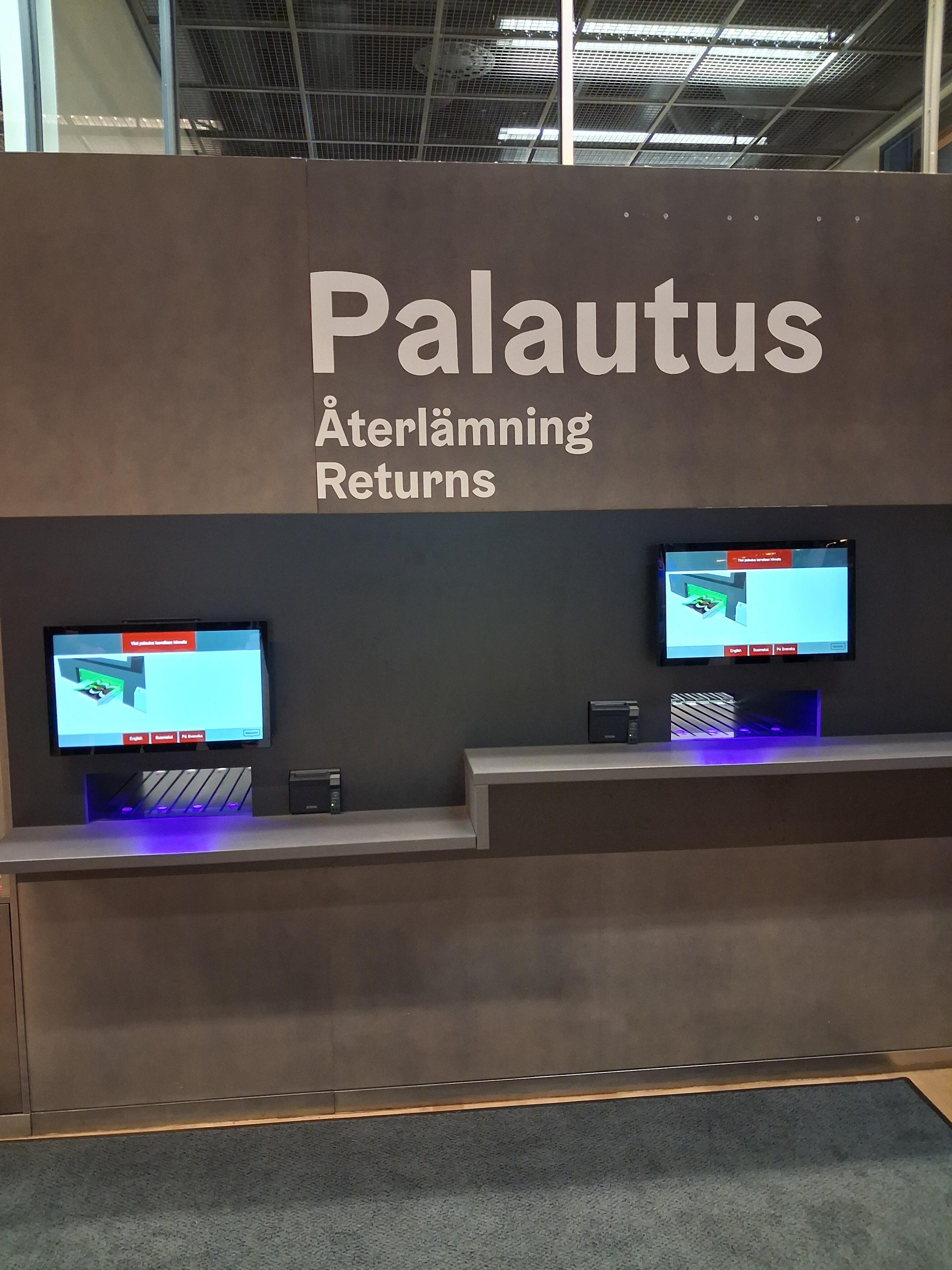 Iso automaatti, jossa on kaksi näyttöä ja teksti palautus, återlämning, returns.