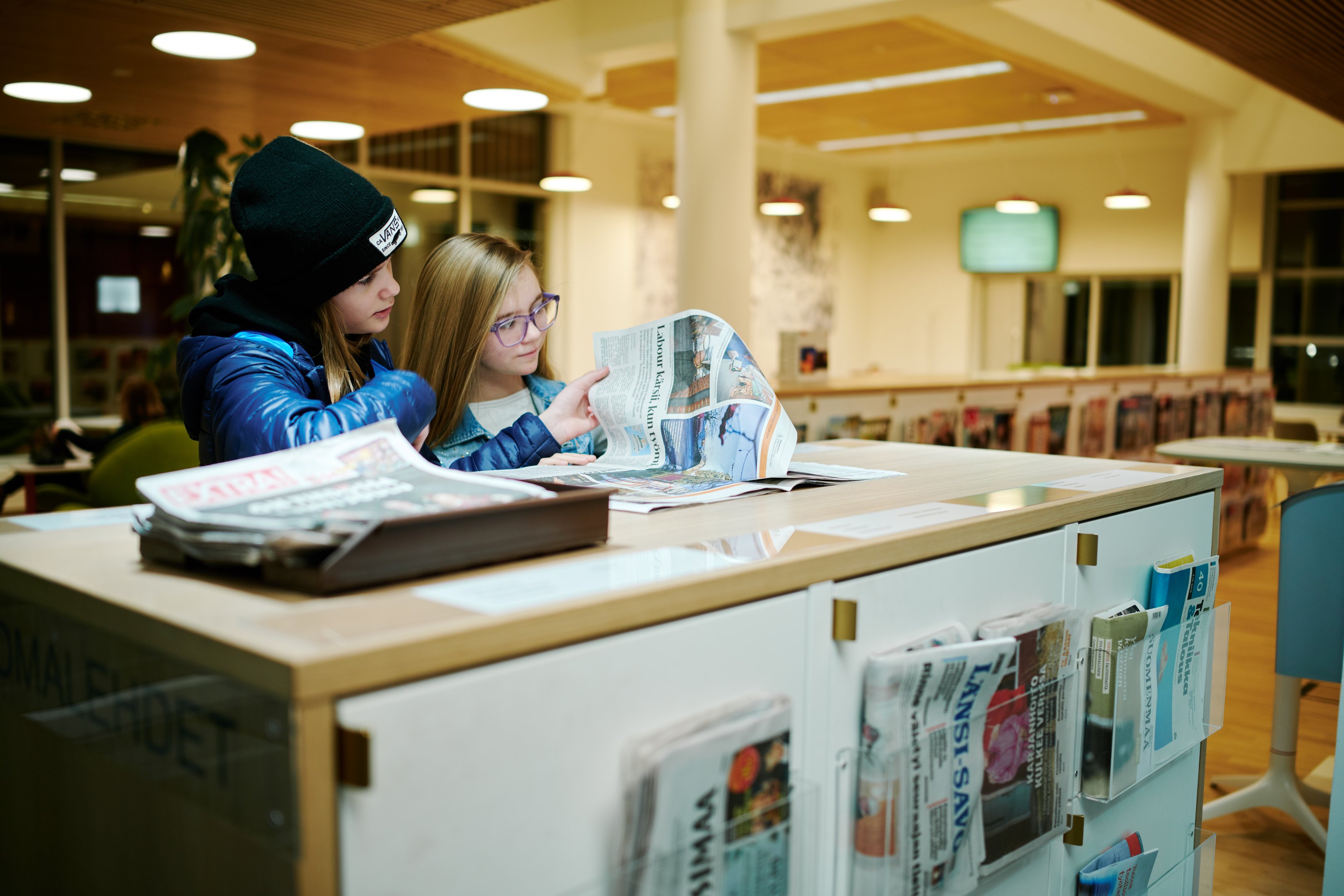 Kaksi lasta selailee lehteä kirjastossa