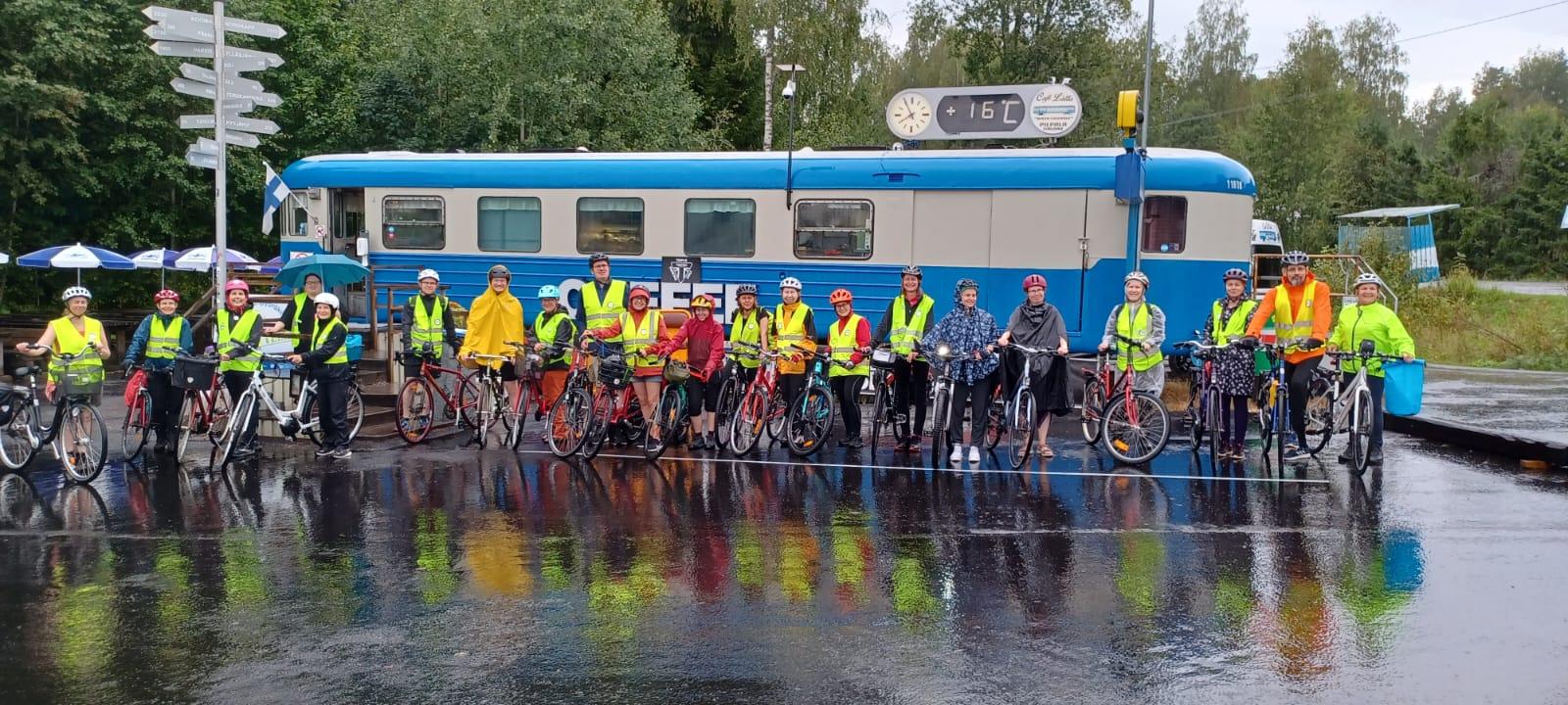 Henkilöitä polkupyörien kanssa junavaunun edessä.
