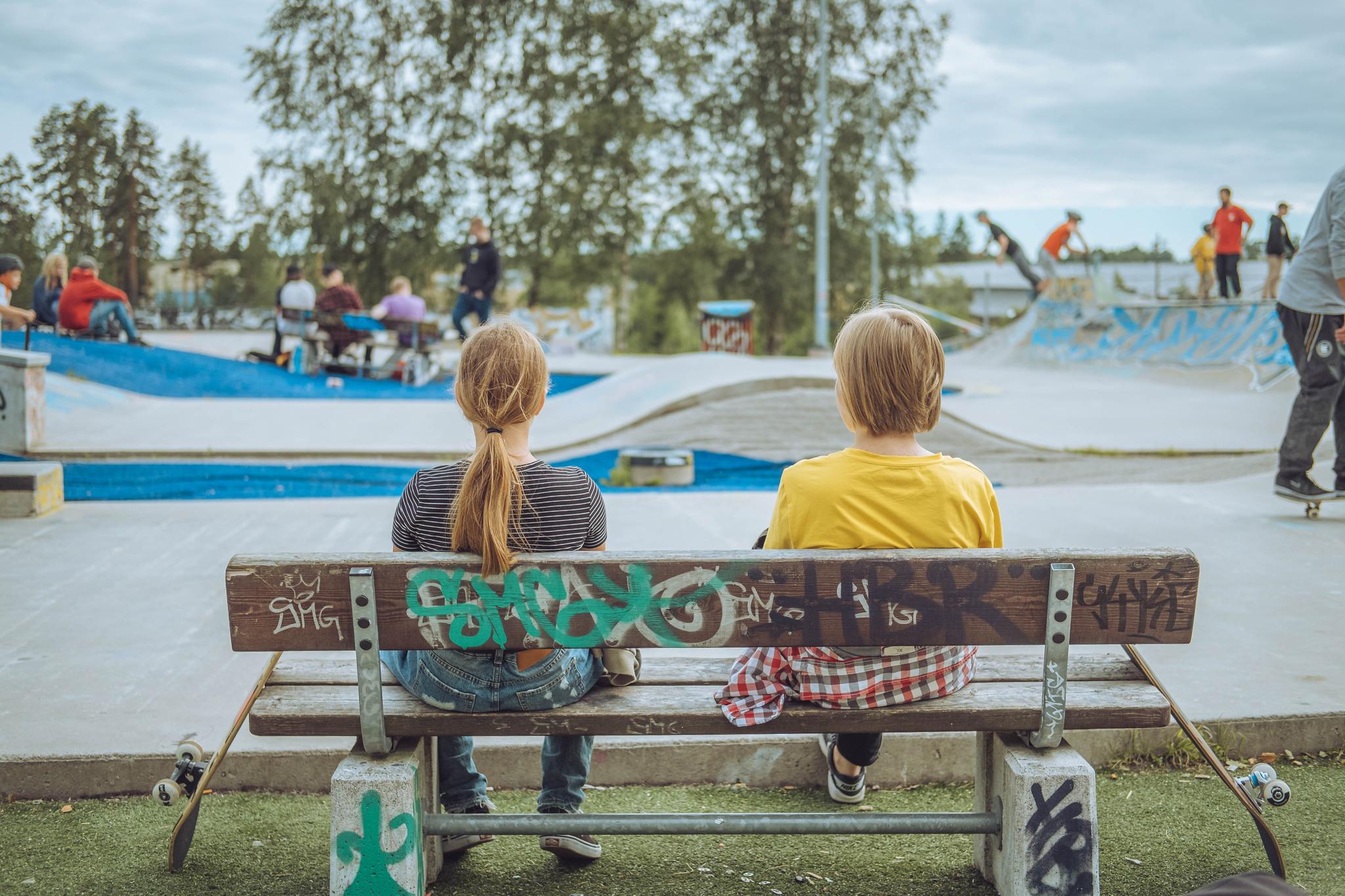 Två unga sitter på bänken i skejtparken.