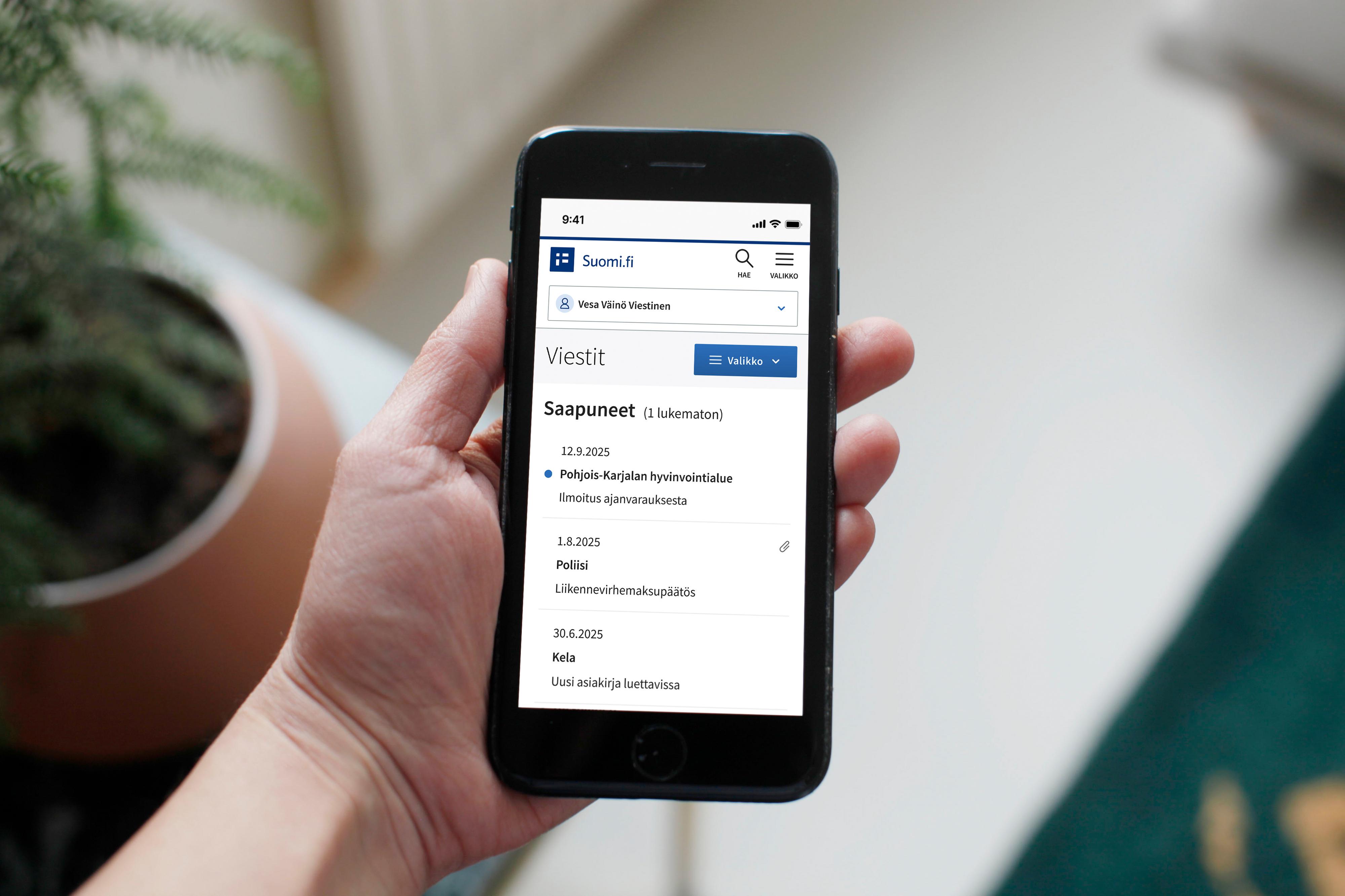 Kännykkä kädessä ja näytöllä Suomi.fi-viestit palvelun saapuneiden viestien kansio.
