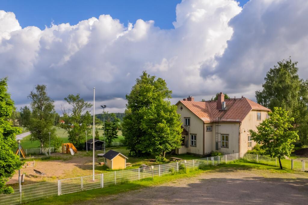 Ett trähus i landsbygdsmiljö med en inhägnad lekplats på gården.