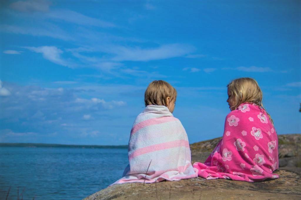 Kaksi lasta istuvat rantakalliolla pyyhkeet ympärillään.